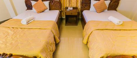 Habitación de hotel con dos camas dobles, cada una con cabecero de madera y colcha amarilla. Entre las camas hay una mesita de noche con una lámpara y un teléfono.