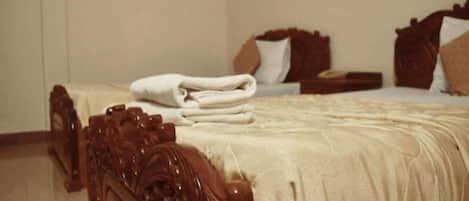 Una cama bien hecha con cabecera de madera, una toalla blanca doblada y una mesita de noche con lámpara.