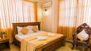 Une chambre d’hôtel avec un lit en bois, une table de chevet, une chaise et des rideaux.