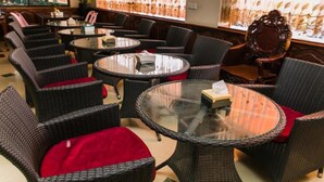 Un restaurant avec des chaises en osier et des tables rondes en verre, dont une chaise est agrémentée d’un coussin rouge.