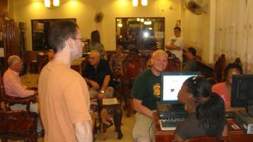 A group of people in a room with wooden furniture, some seated and some standing, with a computer on a table in the foreground.