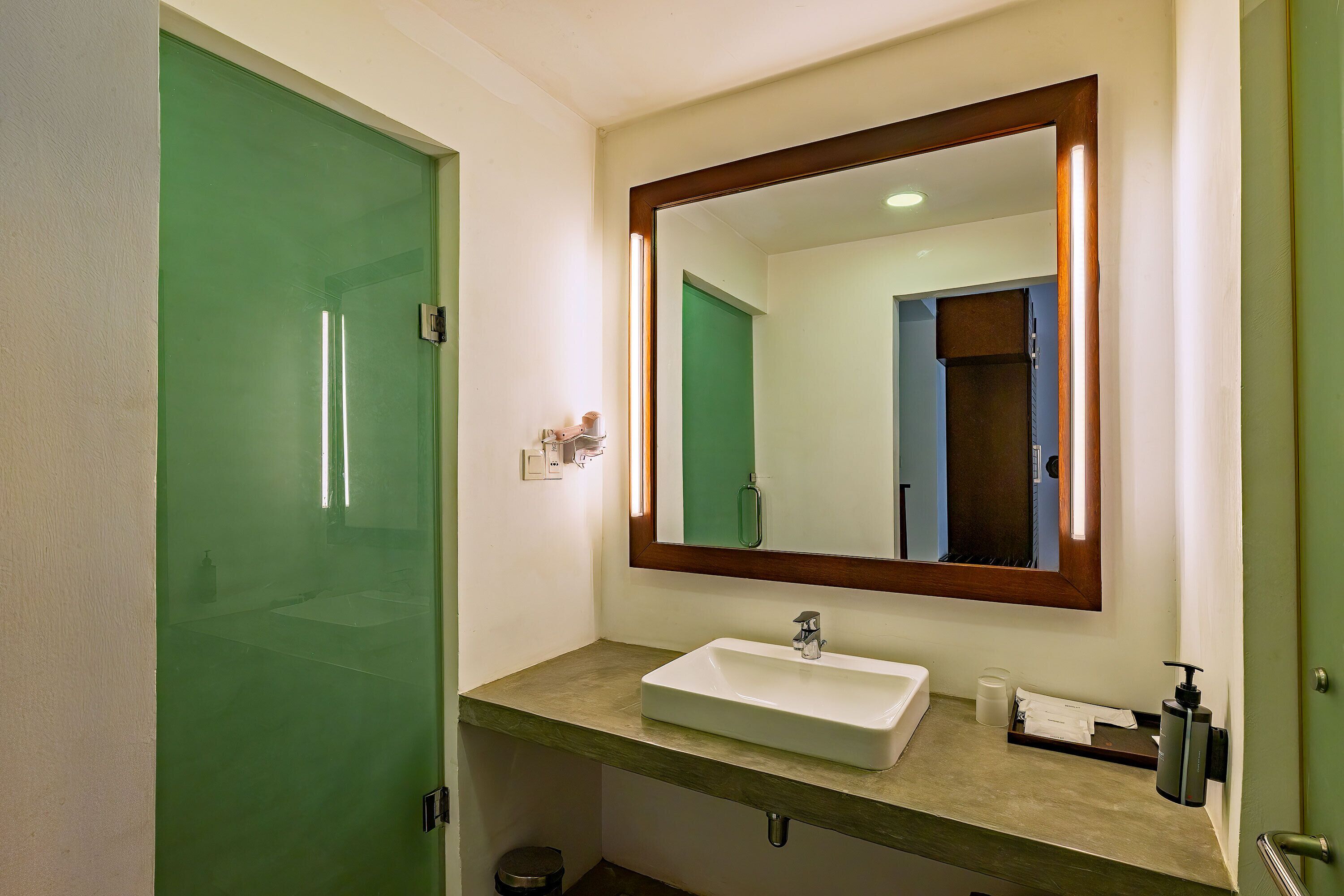 A bathroom with a green door, a white sink, a mirror, and a towel dispenser.