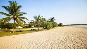 A sandy beach with palm trees, a lifeguard tower, and umbrellas.