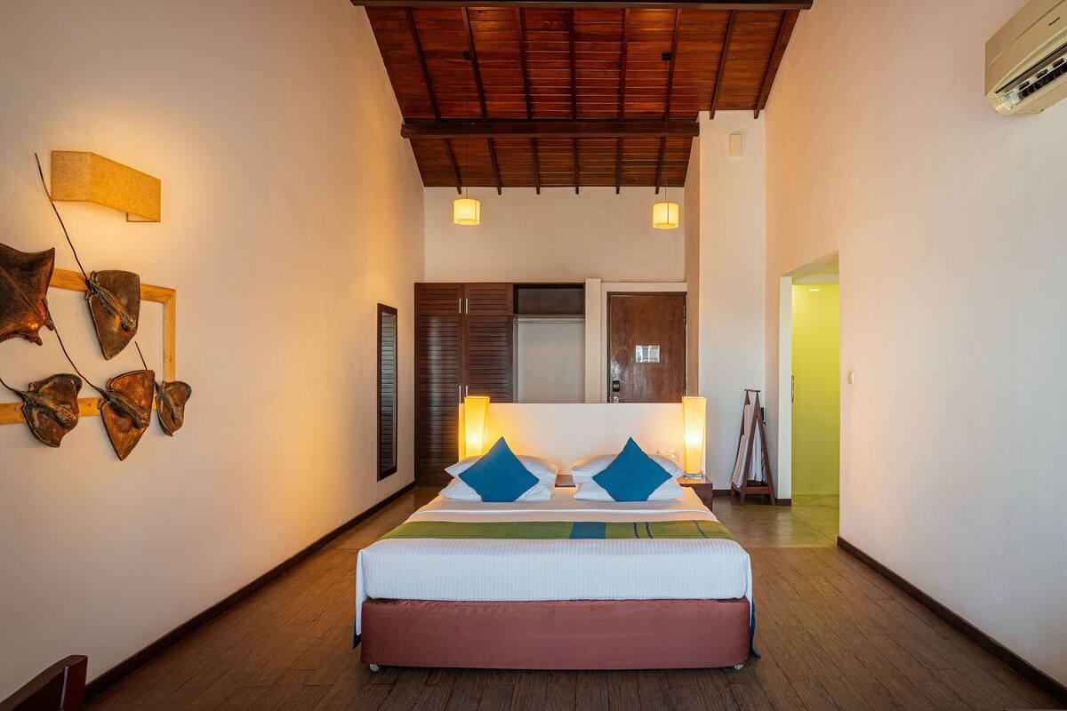 A hotel room with a wooden ceiling, a bed with a red headboard, two bedside lamps, and a wall-mounted artwork.