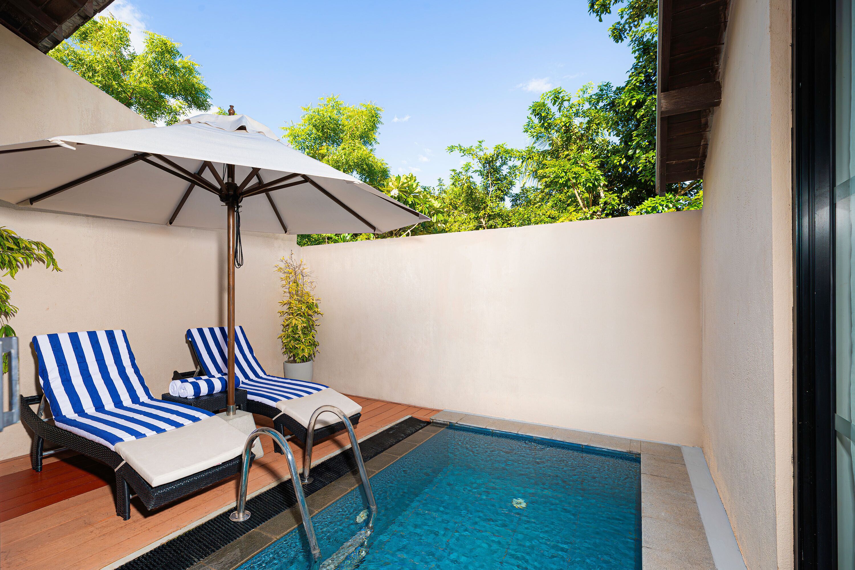 A poolside area with two lounge chairs, a pool, and an umbrella.