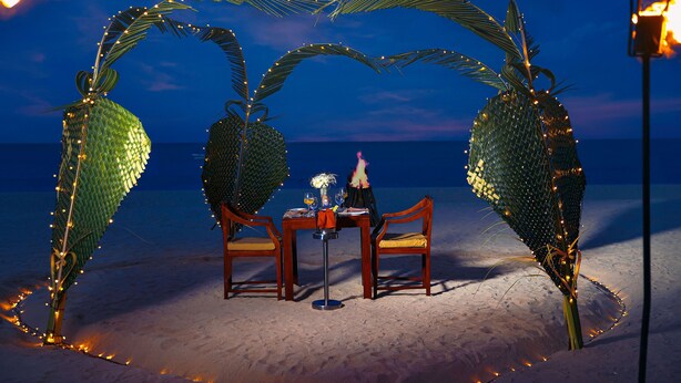 A beach setting with a table and chairs under a decorative archway with string lights.