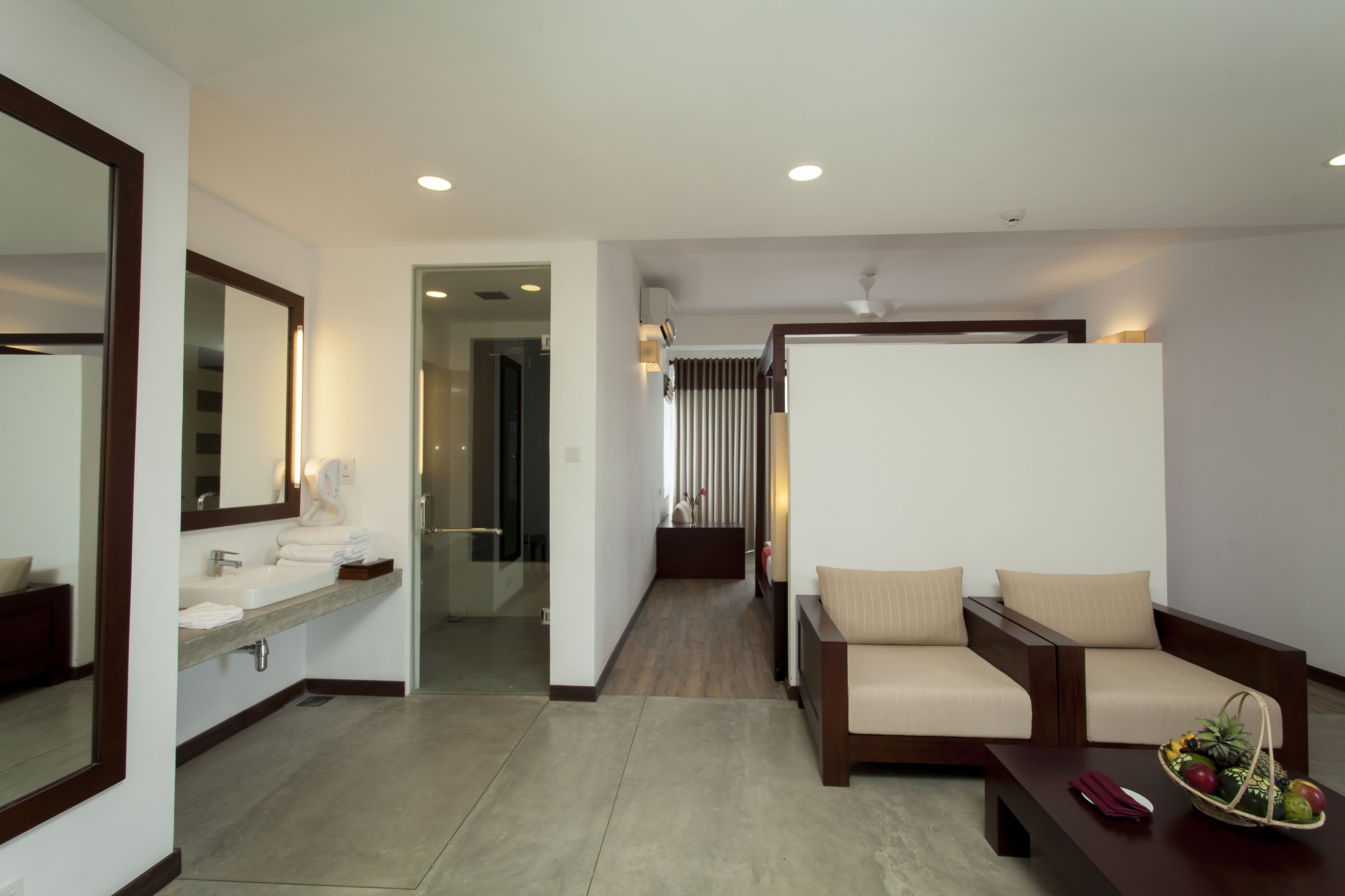A modern hotel room with a large mirror, a sink, a sofa, and a small table with fruit.