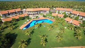 An aerial view of a resort with multiple buildings, a central swimming pool, and surrounding palm trees.