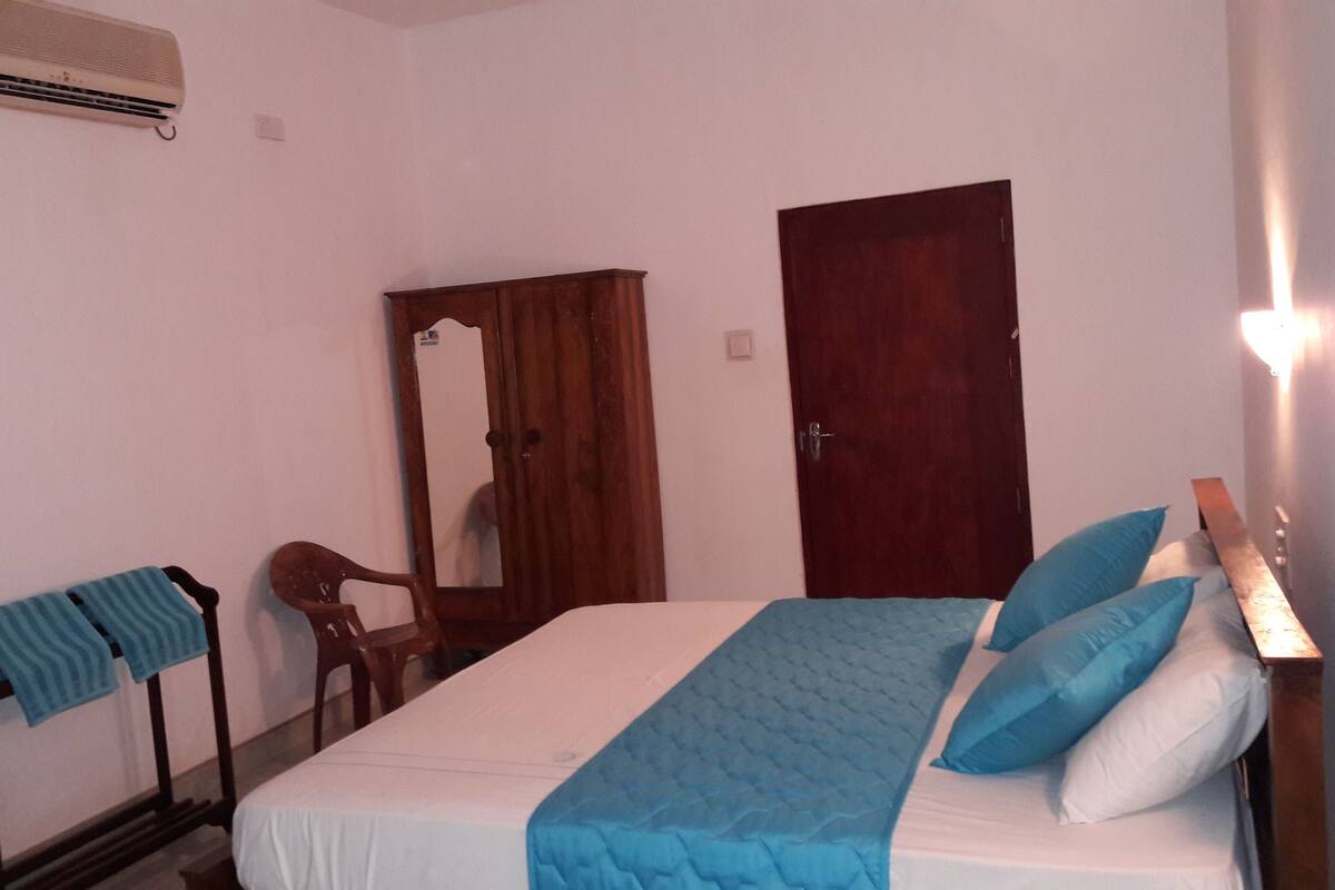 Un dormitorio con una cama, una silla de madera, un armario de madera y un espejo.