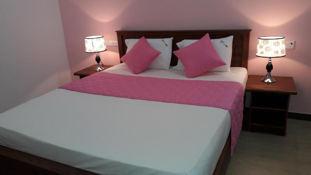 A bed with a white and pink bedspread, two bedside lamps, and a wooden headboard.