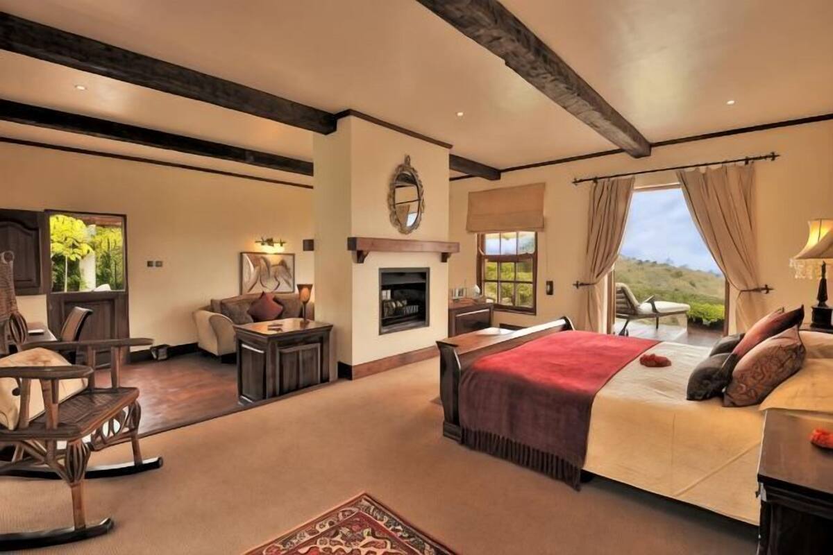 Une chambre avec un grand lit, une cheminée, un canapé et une vue sur l’extérieur.