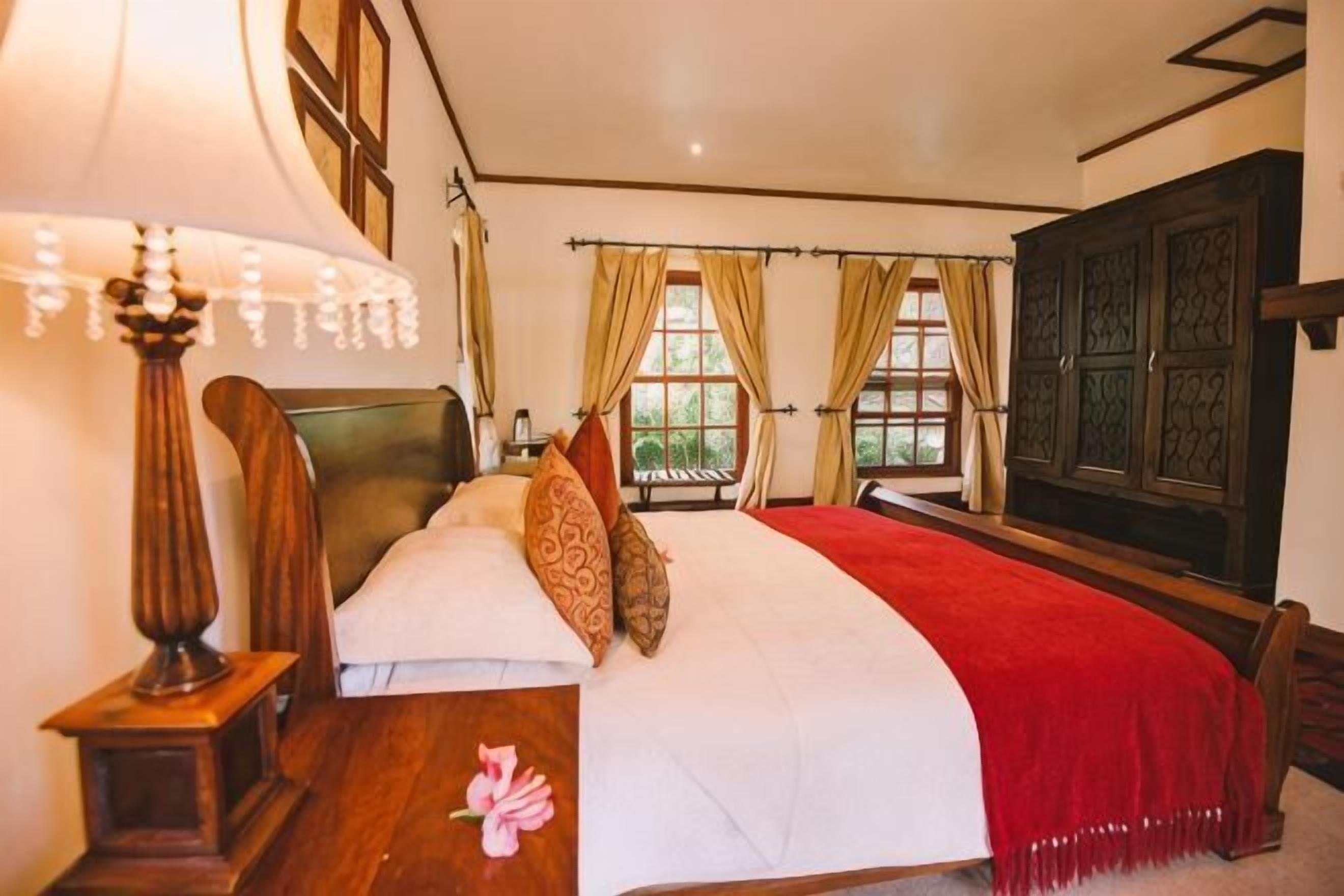 A bedroom with a bed, a nightstand, a lamp, and a window with curtains.