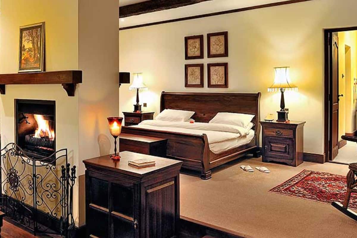 Une chambre d’hôtel confortable avec une cheminée, un grand lit, des lampes de chevet et une tête de lit en bois.