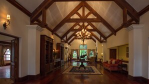A spacious lobby with high ceilings, wooden beams, and a chandelier. There is a red sofa and a wooden coffee table in the center. - Elewana The Manor Ngorongoro (Karatu)