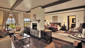 A spacious living room with a fireplace, a large bed, and a cozy seating area. - Elewana The Manor Ngorongoro (Karatu)
