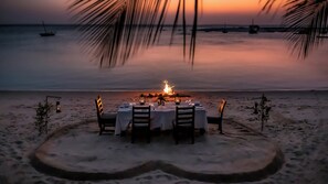 Een diner op het strand, compleet met een tafel, stoelen en een kampvuur in het midden.