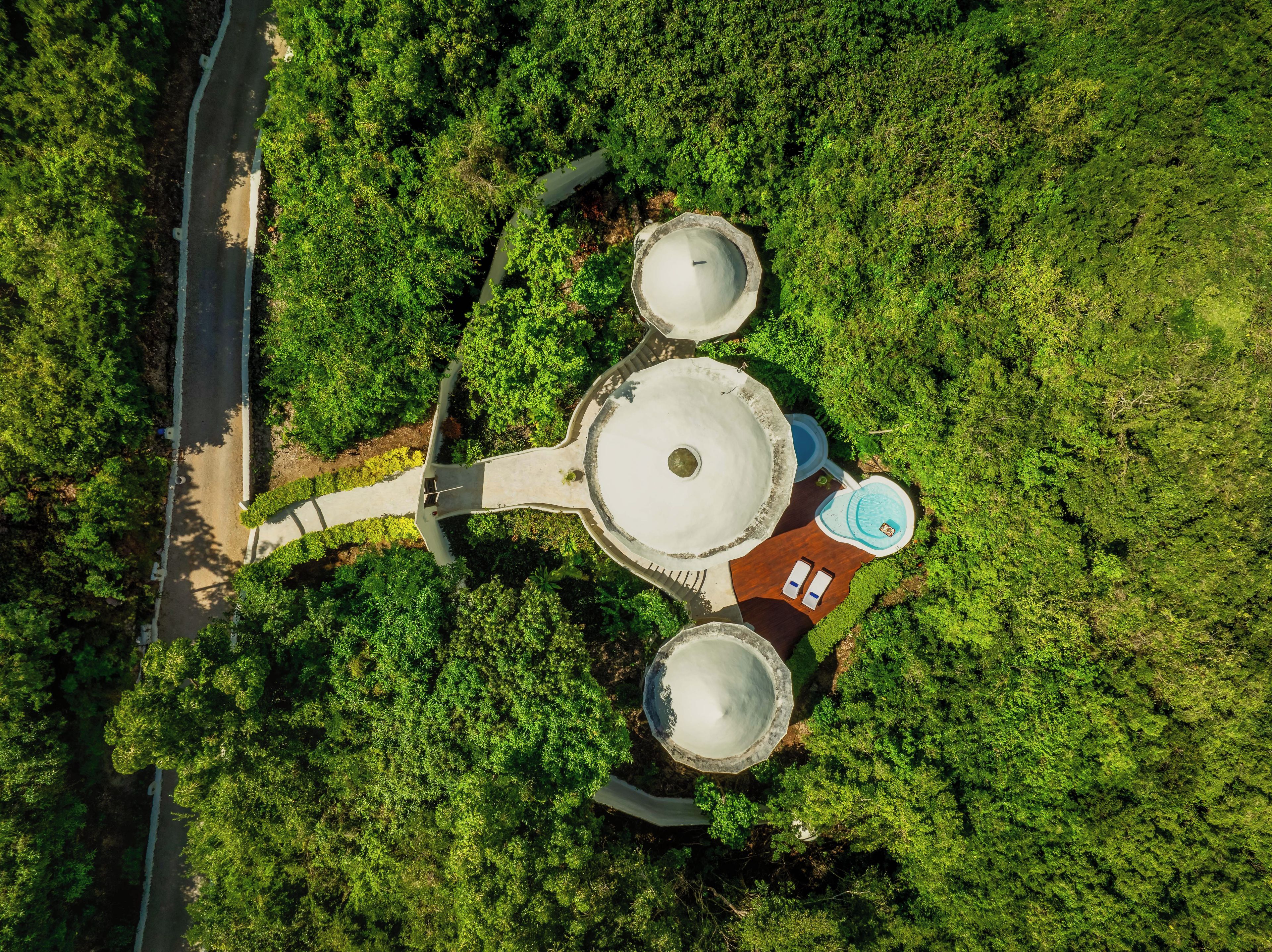 Vista aérea de una propiedad con una estructura circular central, dos estructuras circulares más pequeñas y un edificio rectangular con piscina.