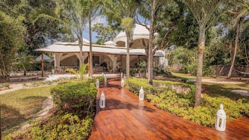A resort with a covered outdoor seating area, a wooden pathway, and lush greenery.
