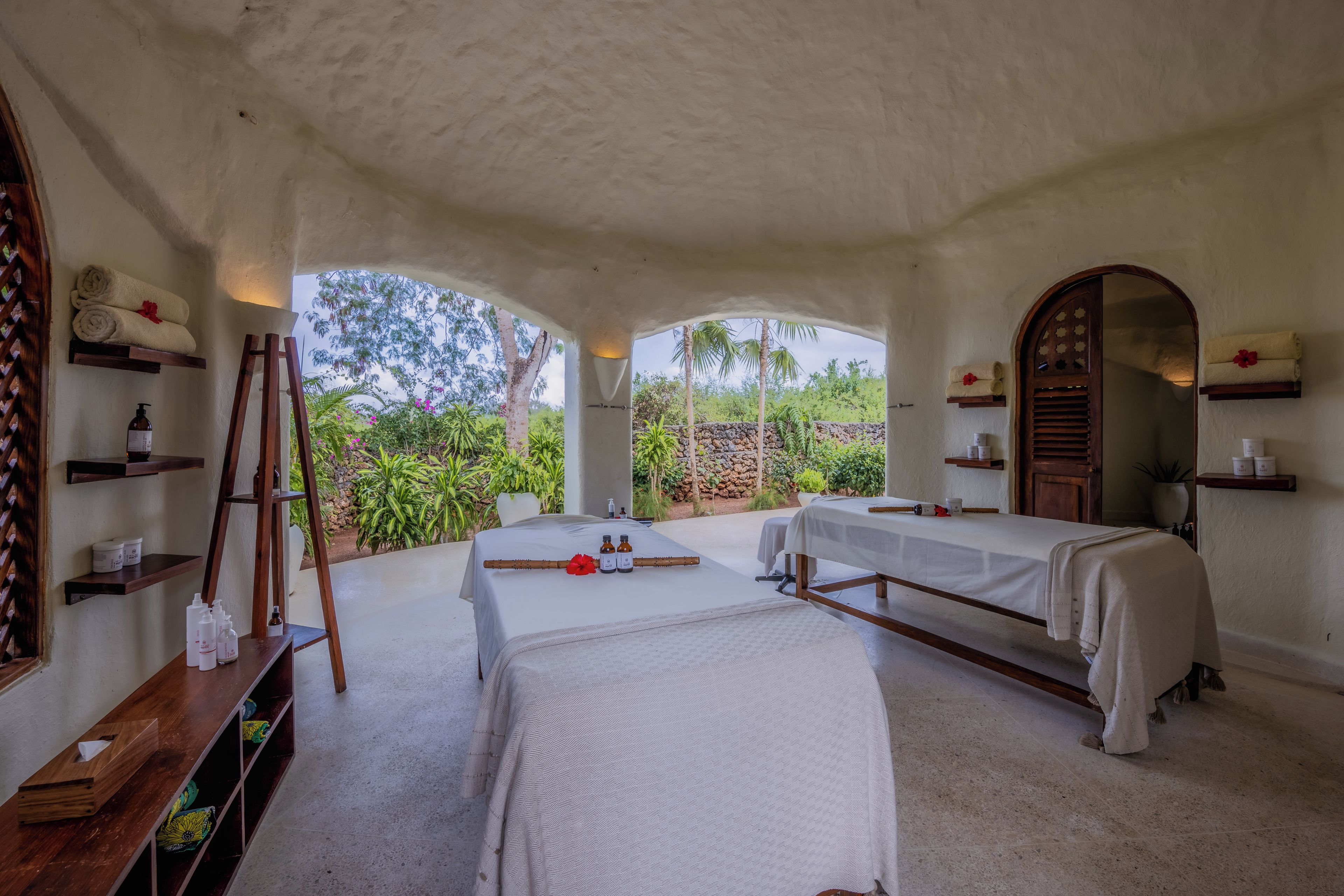 A spa room with two beds, wooden shelves, and a mirror.