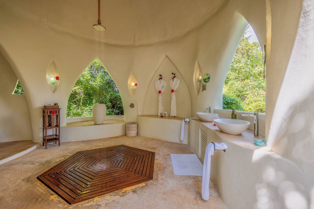 A spacious, naturally lit room with a large wooden floor mat, a white sink, and a window overlooking greenery.