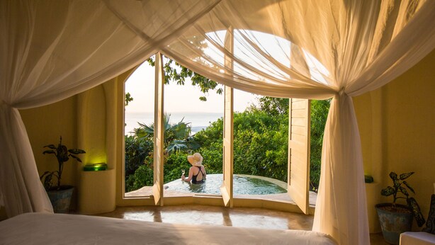 Un dormitorio con un ventanal grande, una cama y vistas a zonas verdes y al agua.