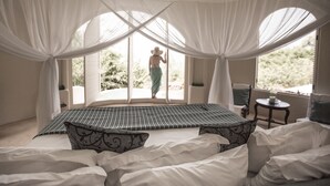 Un dormitorio con una cama grande, cortinas blancas y vistas a espacios verdes.