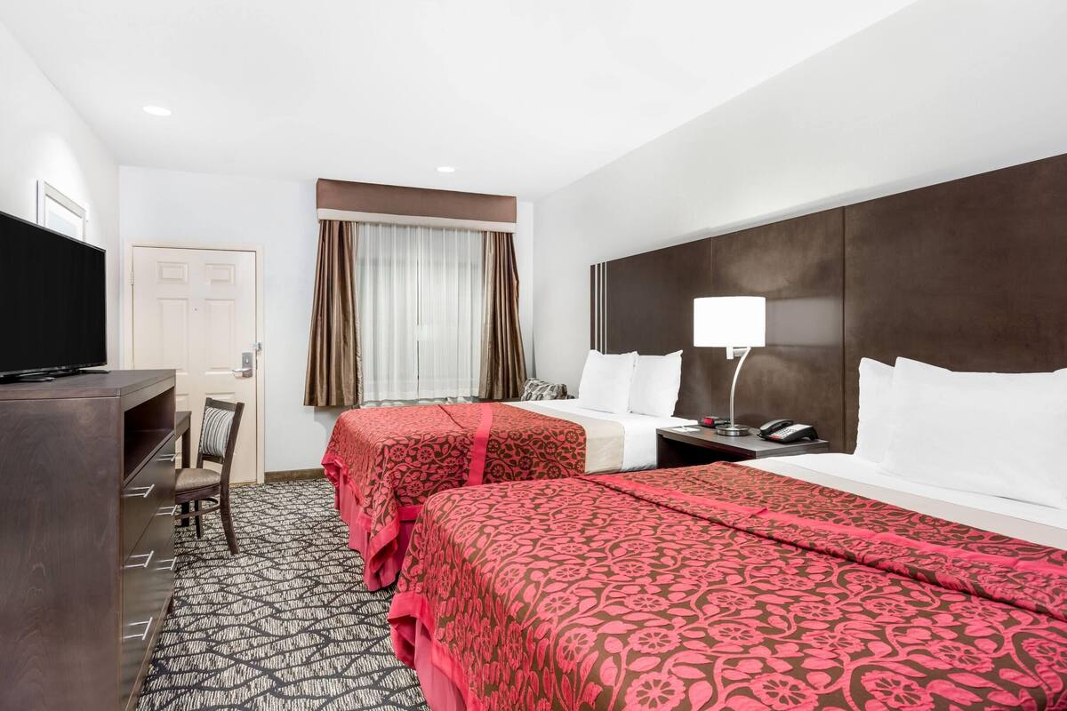 Une chambre d’hôtel avec deux lits, un bureau, une télévision et une fenêtre avec des rideaux.