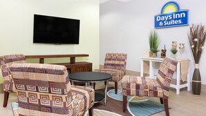 A Days Inn & Suites room with patterned armchairs, a round table, a flat-screen TV, and a sign on the wall. - Days Inn & Suites by Wyndham Madisonville (Madisonville)
