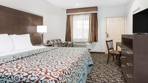 A hotel room with a large bed, a desk, a chair, a television, and a door. - Days Inn & Suites by Wyndham Madisonville (Madisonville)