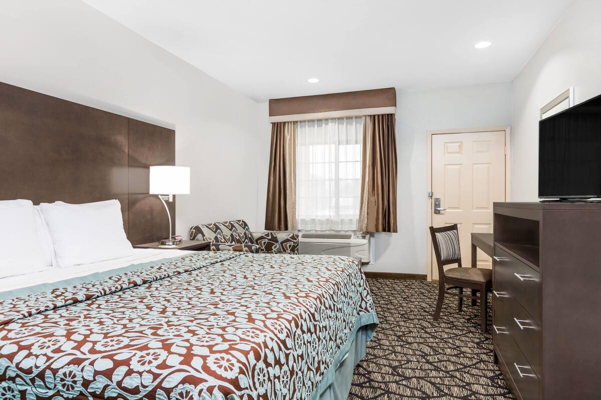 Une chambre d’hôtel avec un grand lit, un bureau, une chaise, une télévision et une porte.