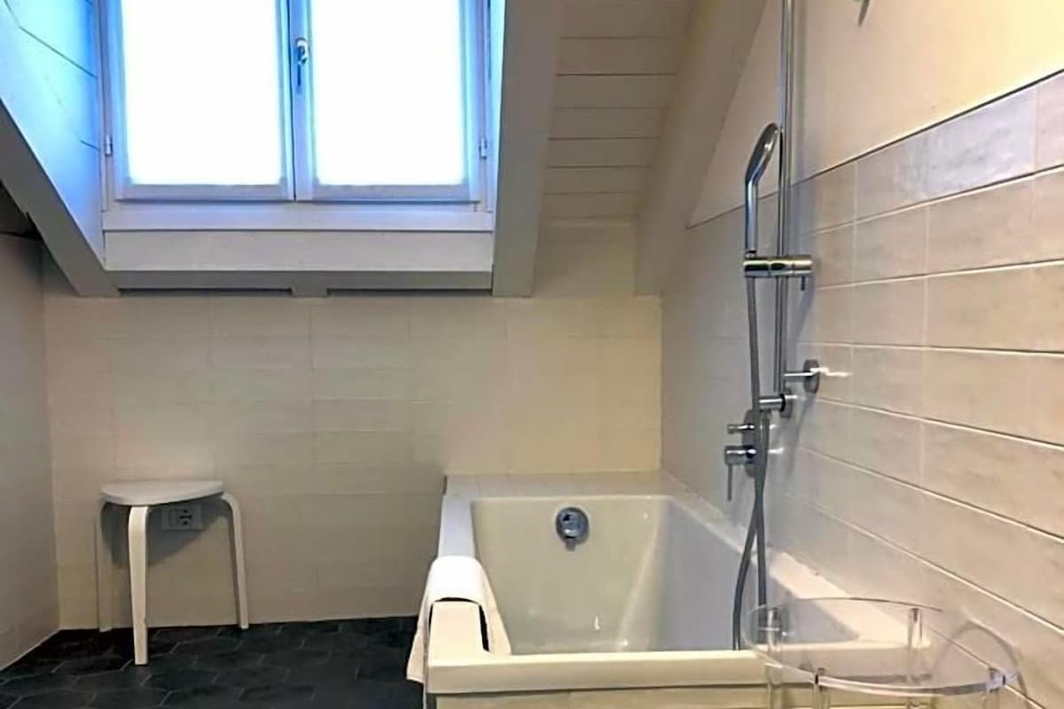 A bathroom with a bathtub, a shower, a small white stool, and a skylight.