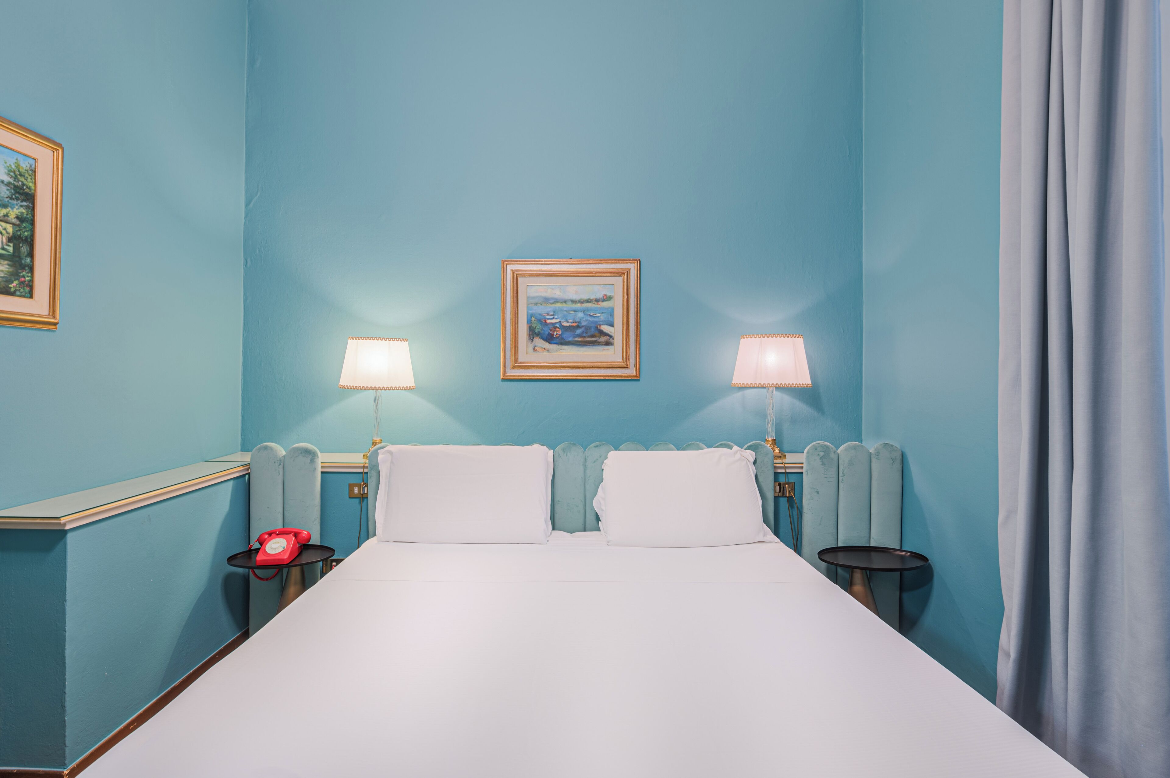 A hotel room with a large bed, two bedside lamps, a painting on the wall, and a telephone on the nightstand.