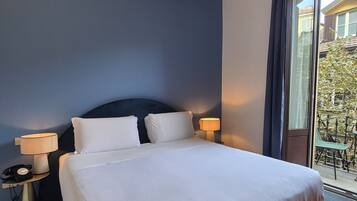 Quarto de hotel com cama, duas luminárias de apoio, telefone e janela com vista para o exterior.