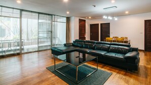 A modern living room with a leather sectional sofa, a glass coffee table, and a view through large windows.