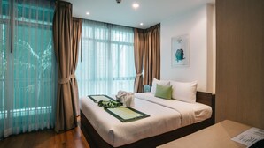 A hotel room with a bed, a wooden floor, and a window with curtains.