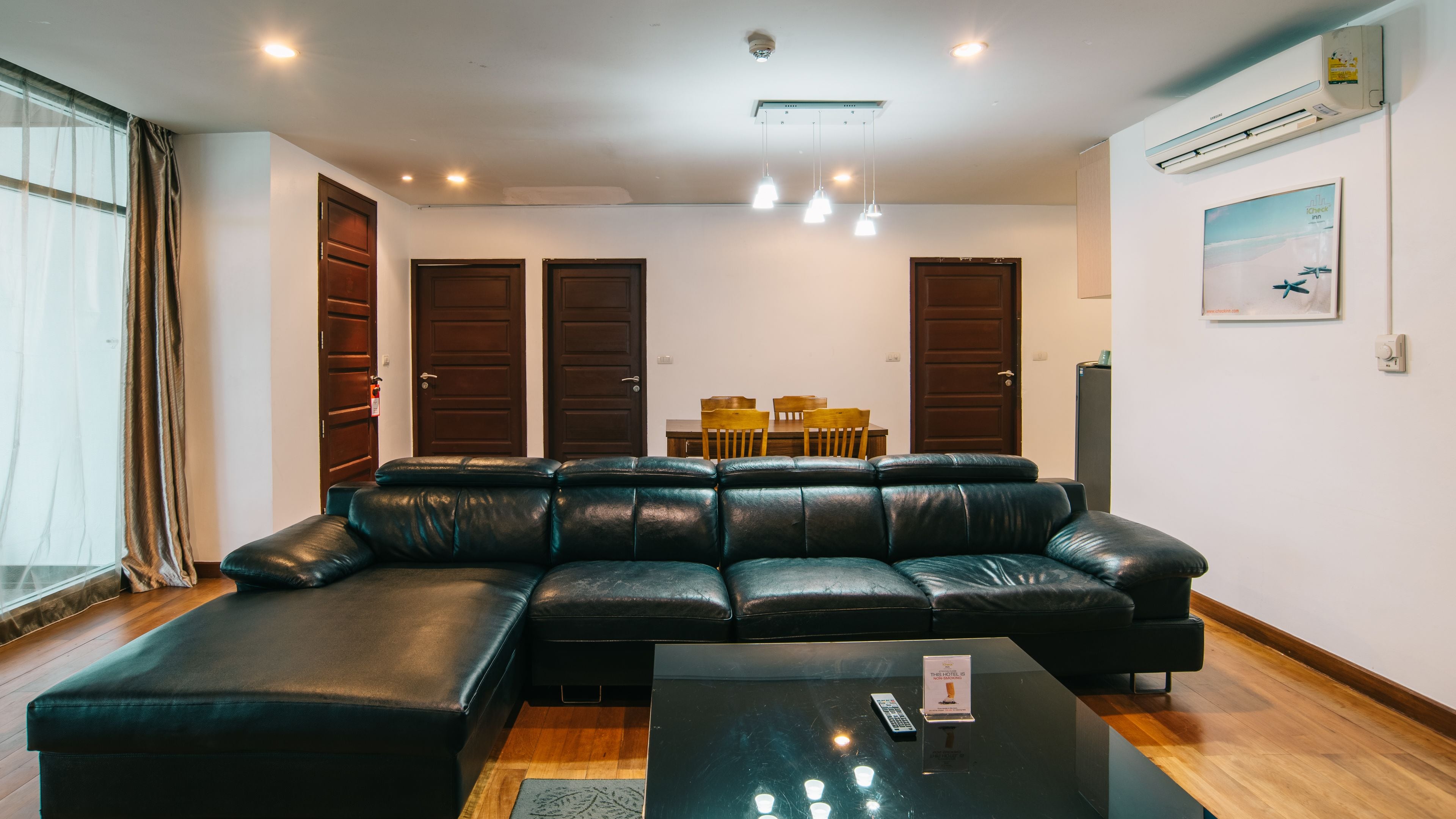 A modern living room with a sectional sofa, a dining table with chairs, and a black coffee table with a remote control.