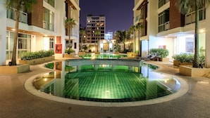 A hotel courtyard with a central swimming pool, surrounded by palm trees and modern buildings.