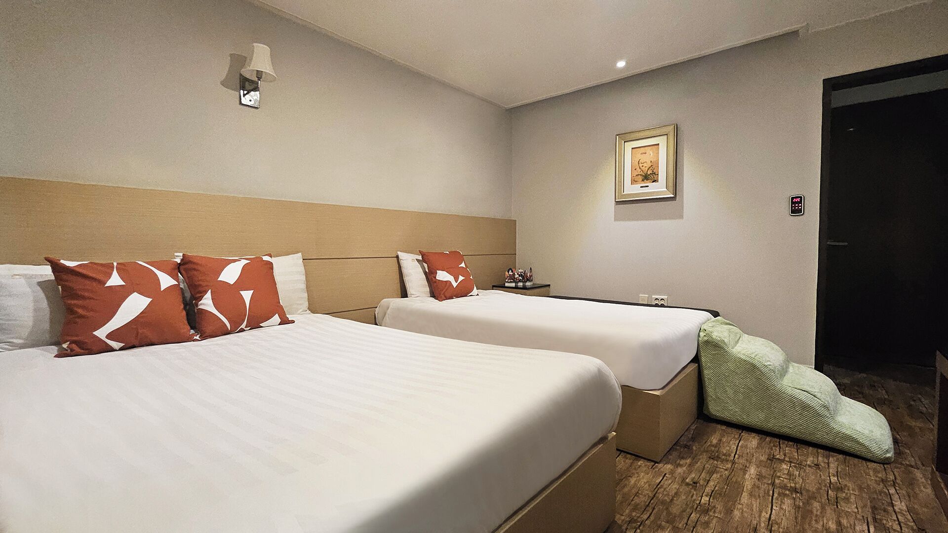 Ein Hotelzimmer mit zwei Betten, einem Nachttisch, einer Lampe, einem gerahmten Bild an der Wand und einer Tür.