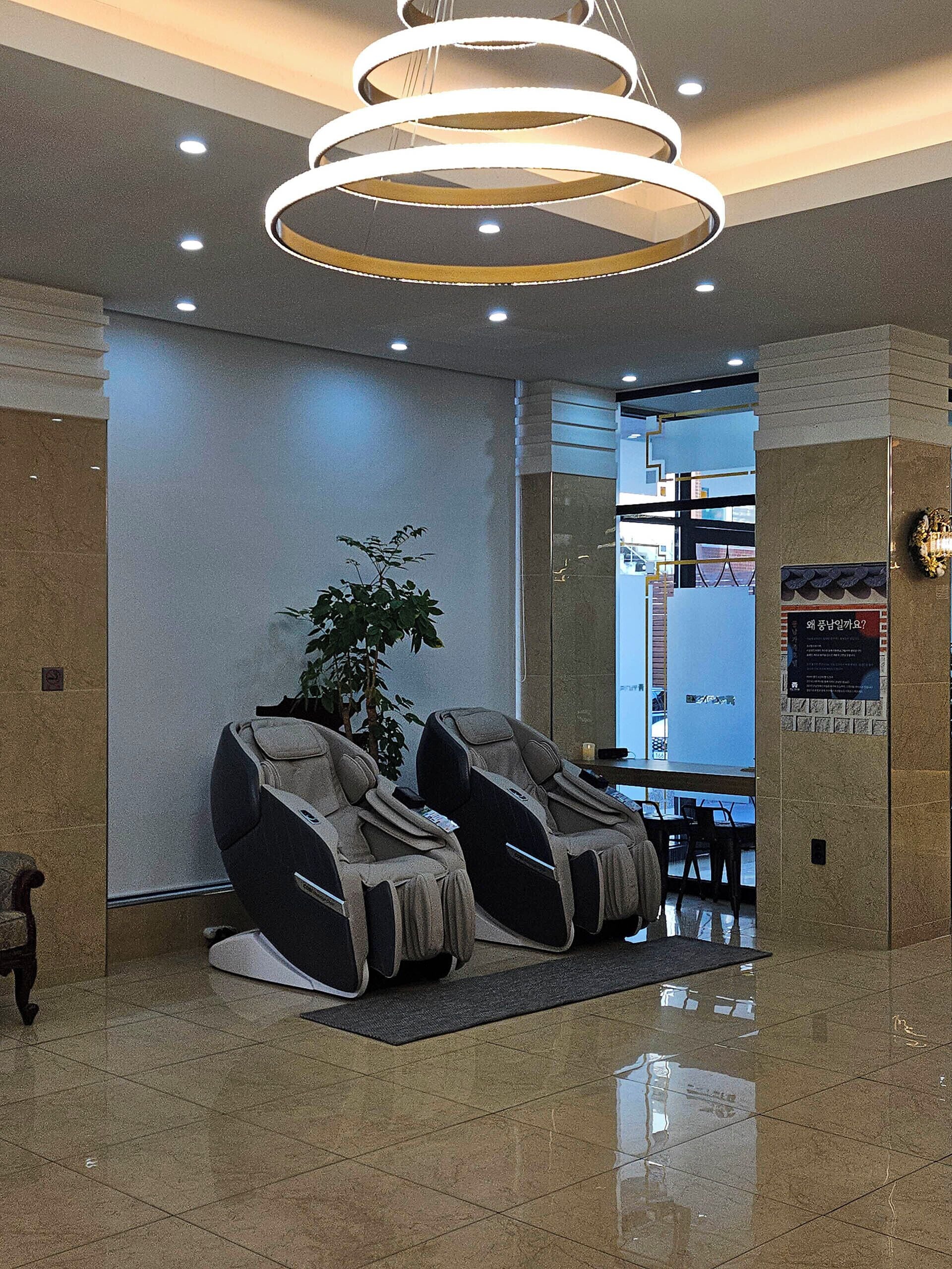 A modern lobby with a massage chair area, a potted plant, and a sign on the wall.