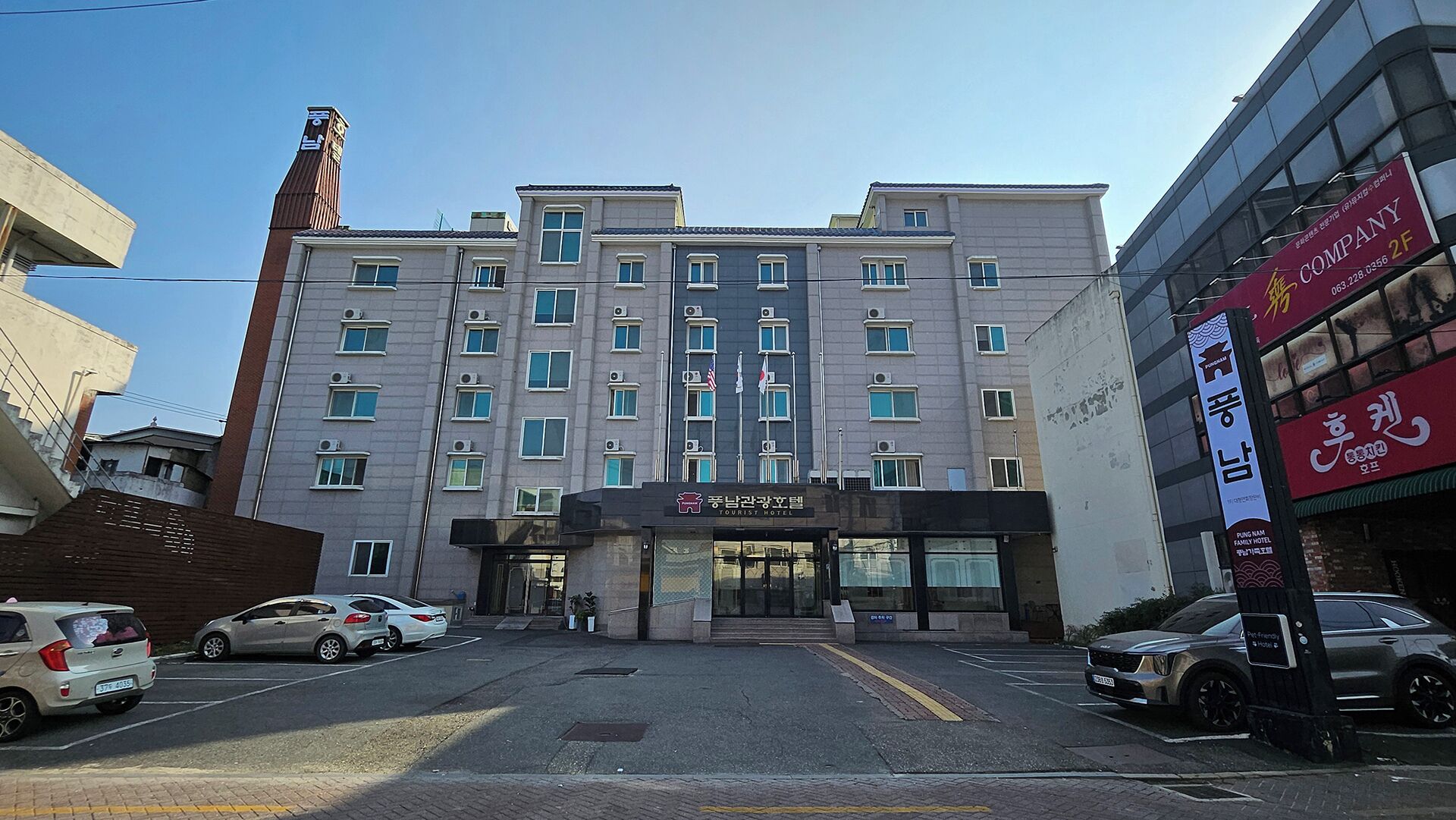 Un hotel de varios pisos con entrada central, varias ventanas y un estacionamiento con coches.