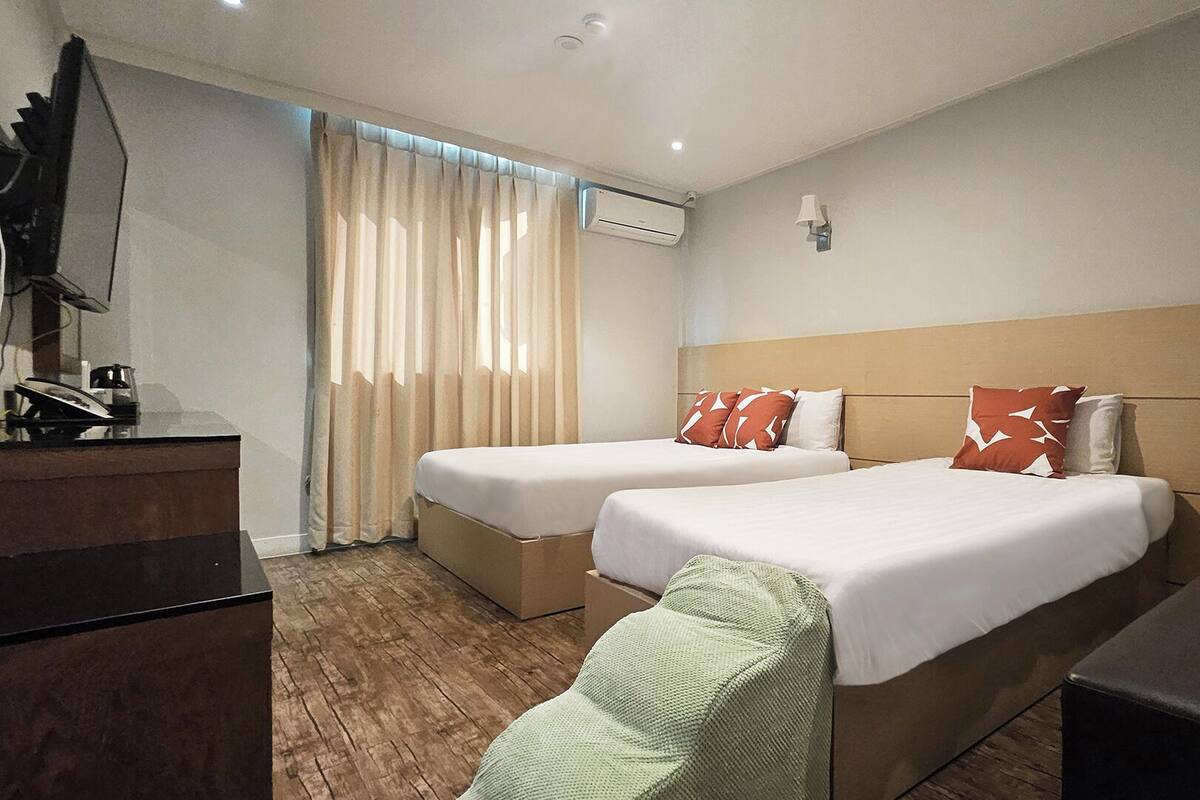 A hotel room with two beds, a desk, a chair, an air conditioning unit, and a television.