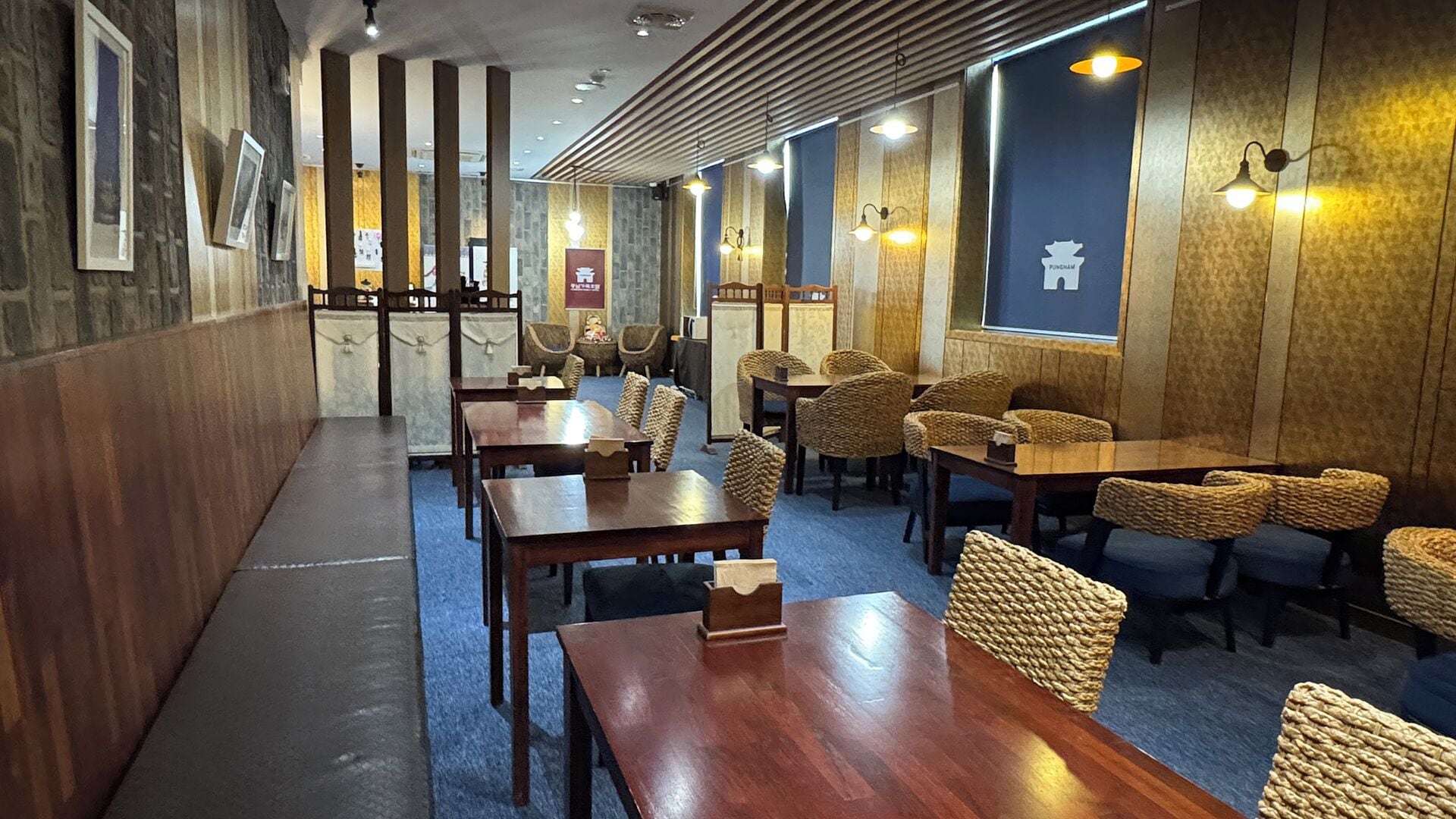 Un restaurante con mesas de madera y sillas tejidas, una alfombra azul y una pared con un letrero.