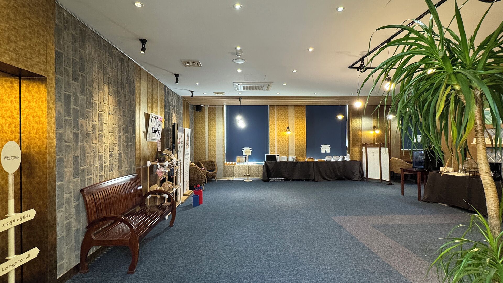 A spacious lounge area with a wooden bench, a small table, and a plant.