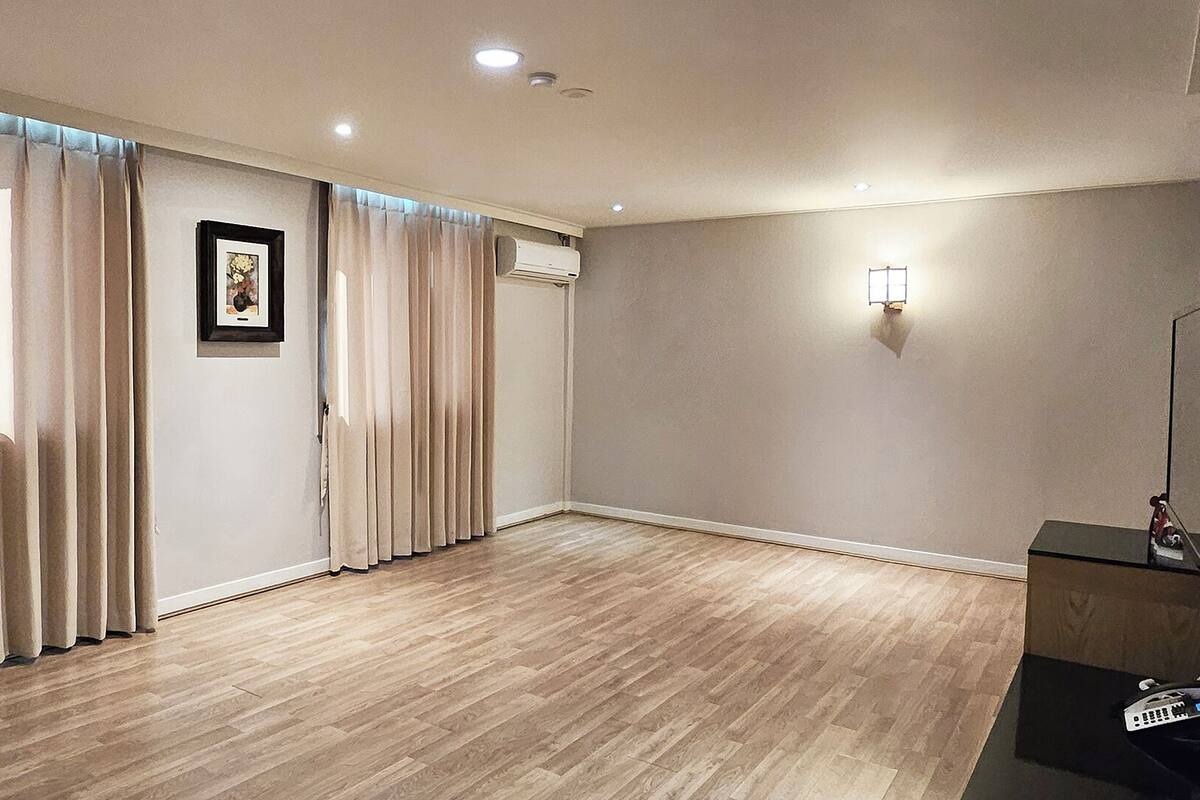 A room with wooden flooring, beige curtains, a framed picture on the wall, and a wall-mounted light fixture.
