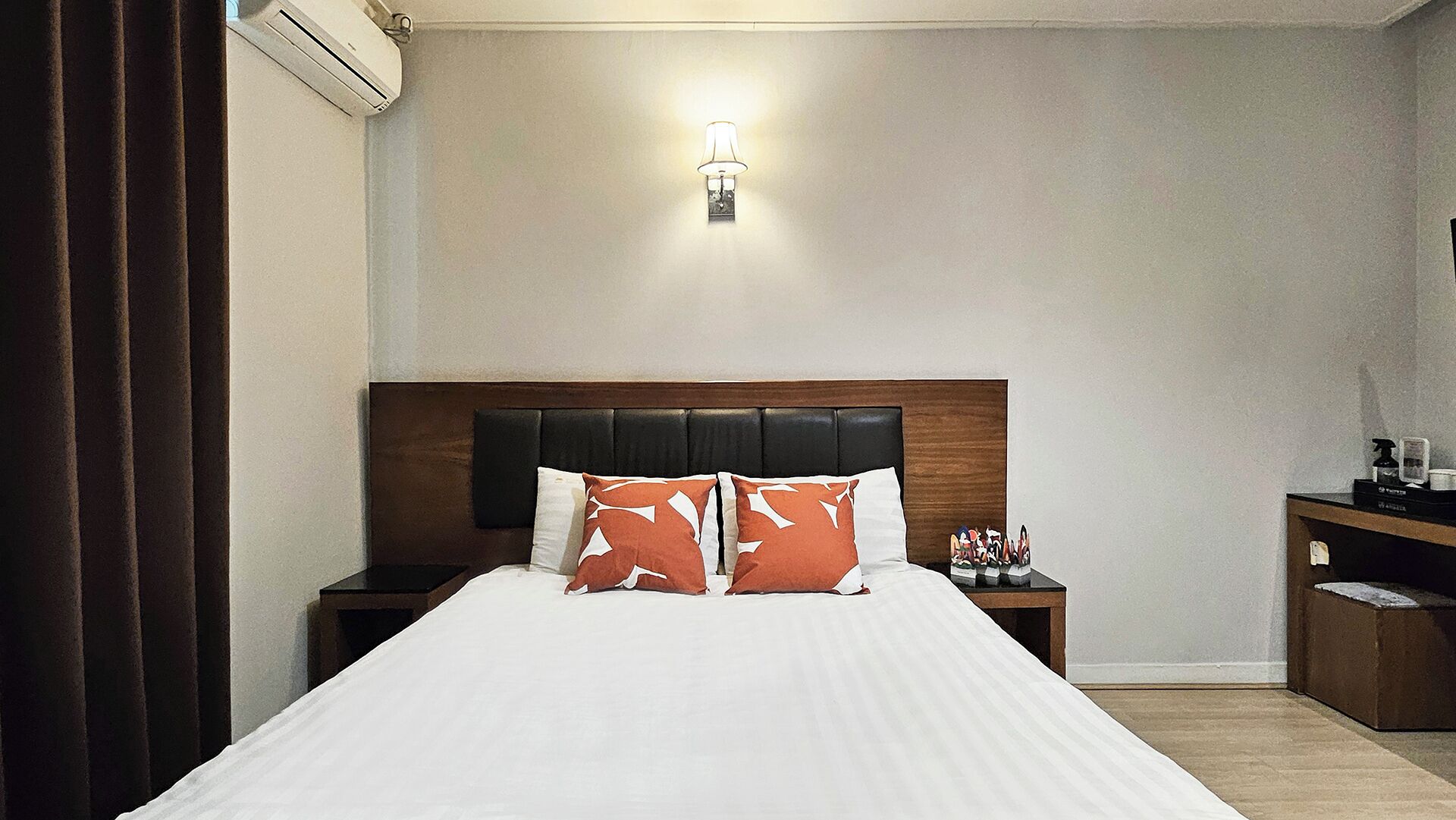 Una habitación de hotel con una cama grande, cabecera, mesita de noche y una lámpara de pared.