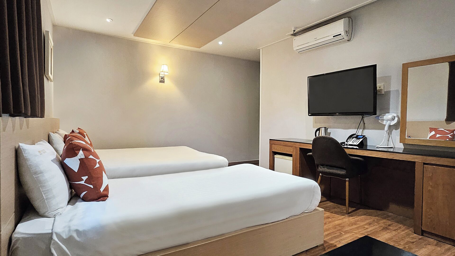A hotel room with two beds, a desk, a chair, a television, and an air conditioning unit.