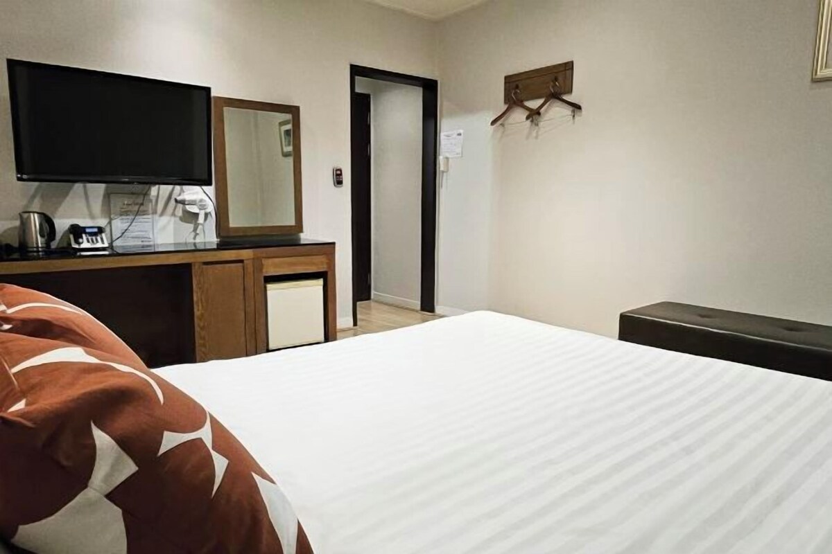 Ett hotellrum med en säng, ett skrivbord med en platt-TV, en spegel och en klädställning.