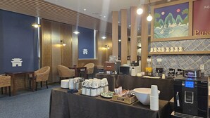 Un espace d’accueil d’hôtel comprenant un coin café, un espace salon et un mur orné d’une œuvre d’art encadrée.