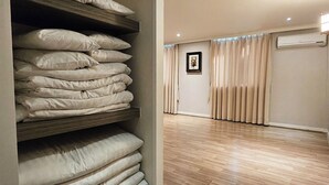 Une pièce avec un plancher en bois, une pile d’oreillers, un tableau encadré au mur et une fenêtre avec des rideaux.