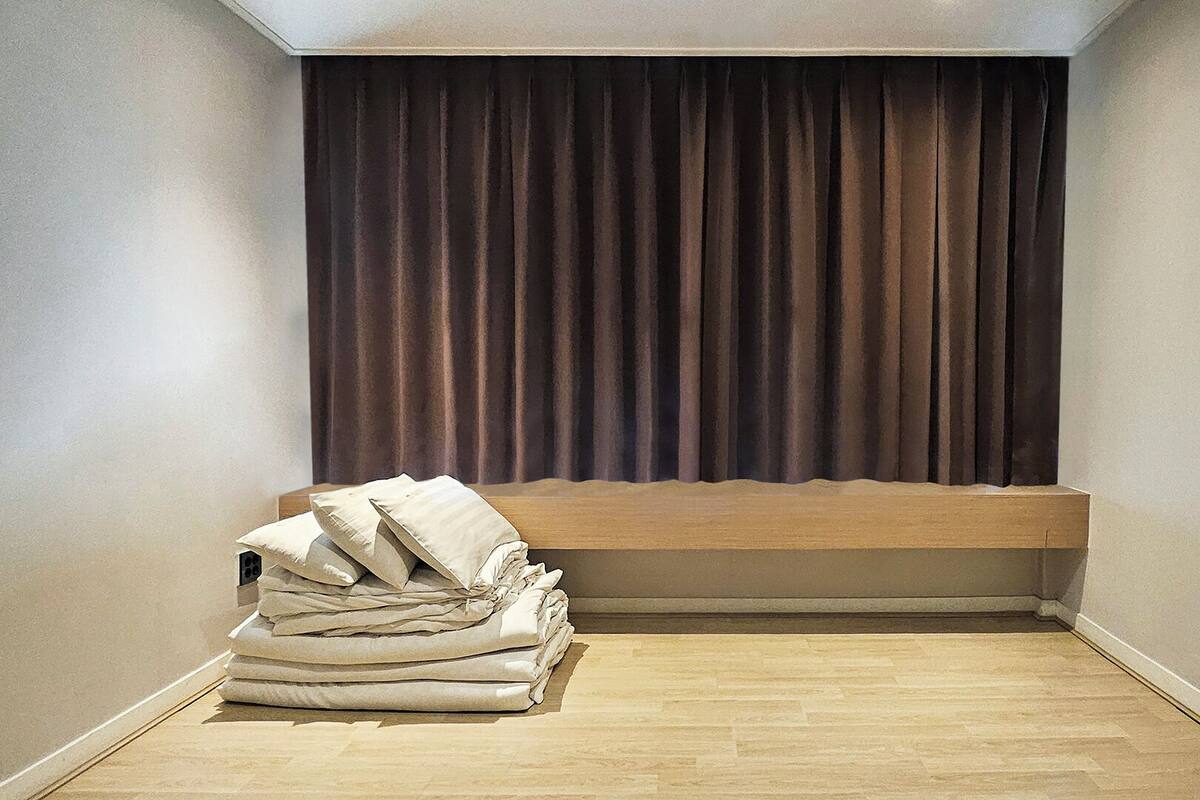 A corner room with a wooden bench, a stack of folded blankets, and a dark curtain.